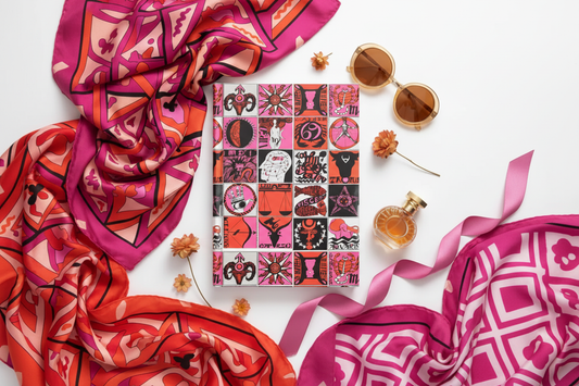 Psychedelic zodiac journal with 12 astrology signs mosaic in pink and red, surrounded by three Pucci-style silk scarves, dried flowers, round sunglasses and vintage perfume bottle - LeBonJournal