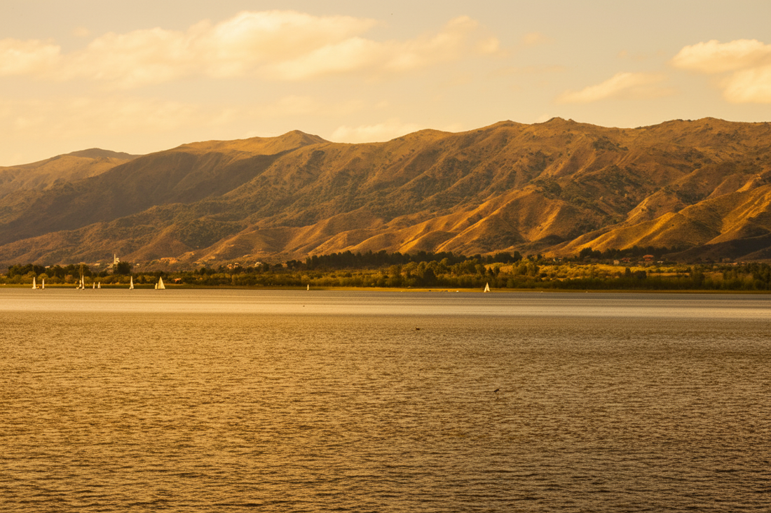Sierras de Córdoba at golden hour with lake and sailboats in the foreground, rolling hills and native vegetation
