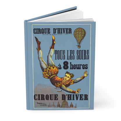 Hardcover circus journal standing upright showing front cover with 1890 Cirque d'Hiver Paris poster featuring aerialist floating above Parisian skyline with hot-air balloon on matte finish cover - LeBonJournal