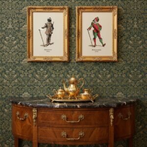 Two framed Maurice Sand Commedia dell'Arte character prints in ornate gold frames hang side by side on a green damask wallpaper wall, positioned above a marble-top wooden console table with a brass tea set.
